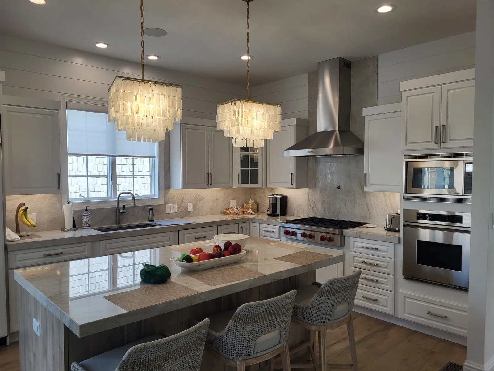 Stone island under tiered chandeliers with white shaker cabinets