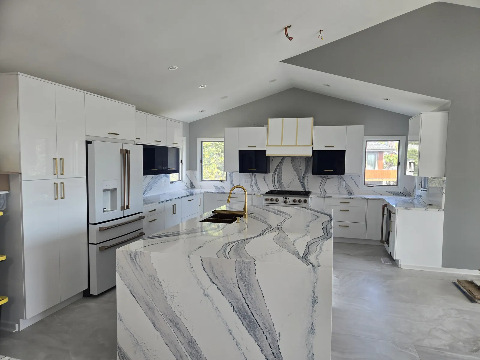 Vaulted white kitchen with a veined stone waterfall island and full height slab backsplash