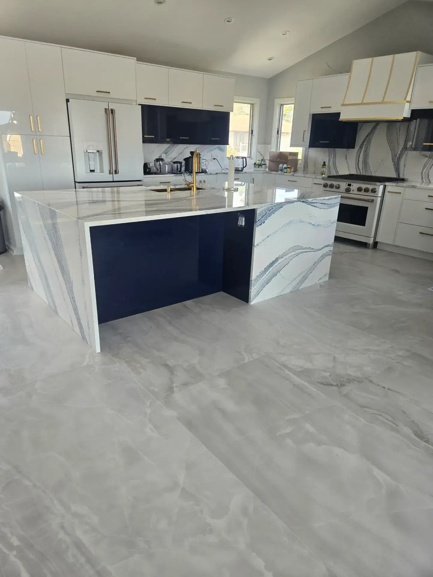 Navy waterfall island with a veined stone top and matching stone floor