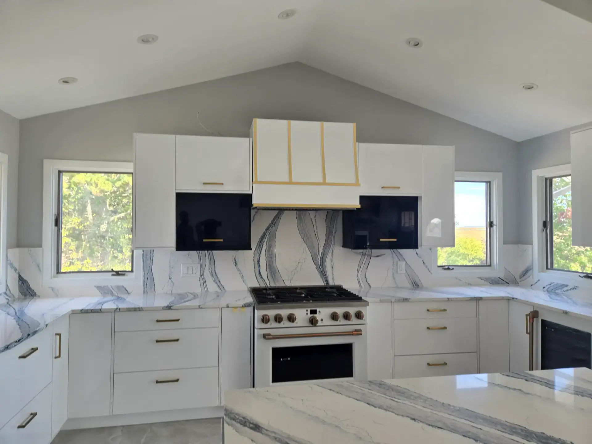 Bookmatched veined slab backsplash behind a range in a white kitchen